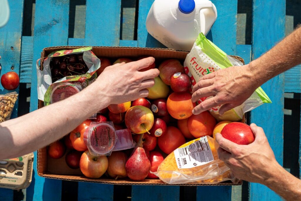 several hands reaching into a box of fresh fruit at food pantry