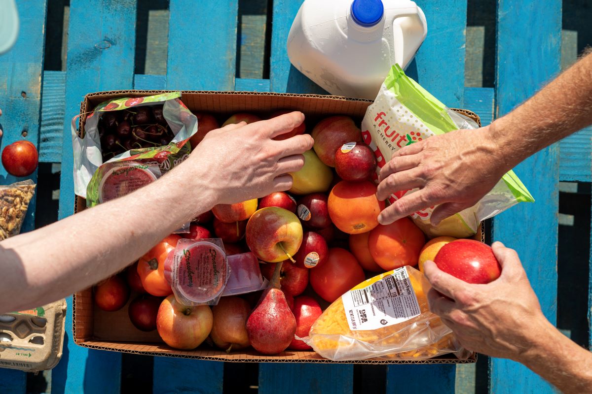 several hands reaching into a box of fresh fruit at food pantry
