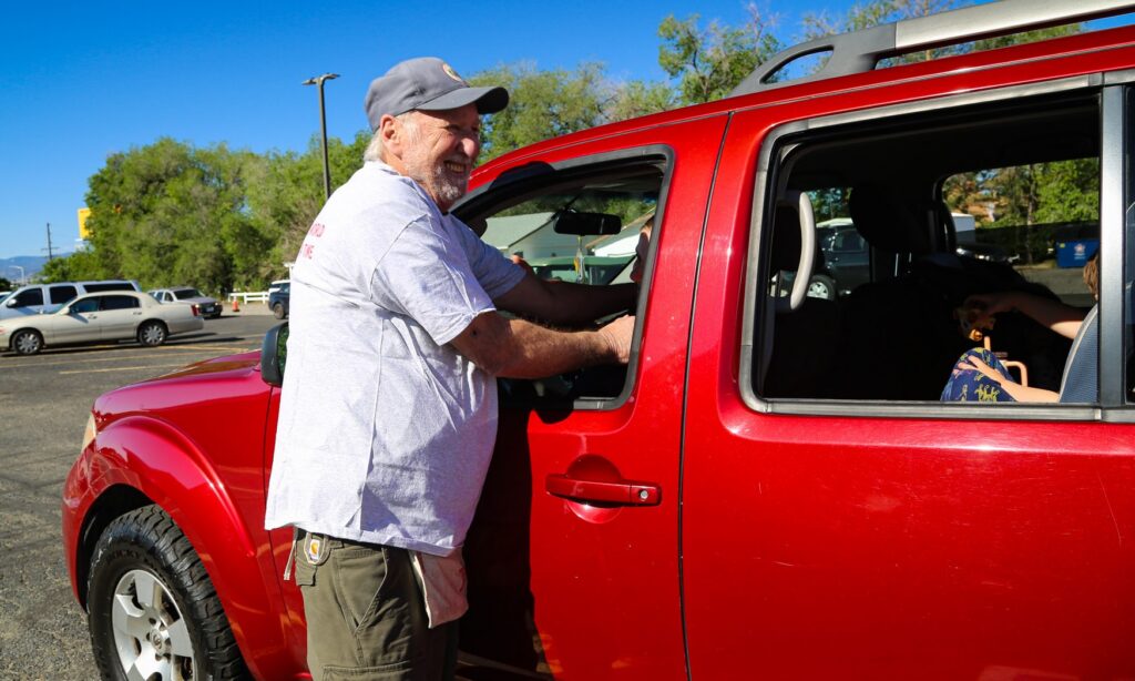 man standing by red car laughs with customer at food bank