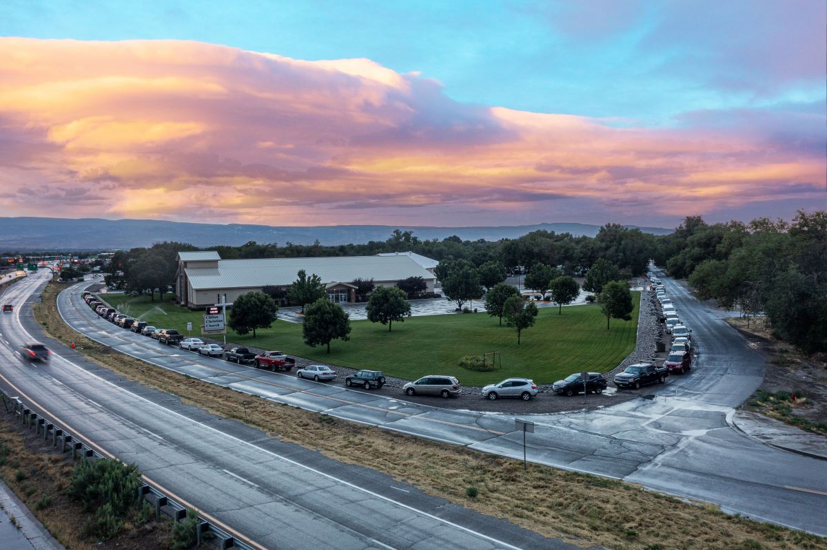 long line of cars curving around a corner in front of a church food bank at sunrise
