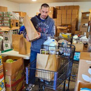 man carrying paper bag of food with full shopping cart at food pantry