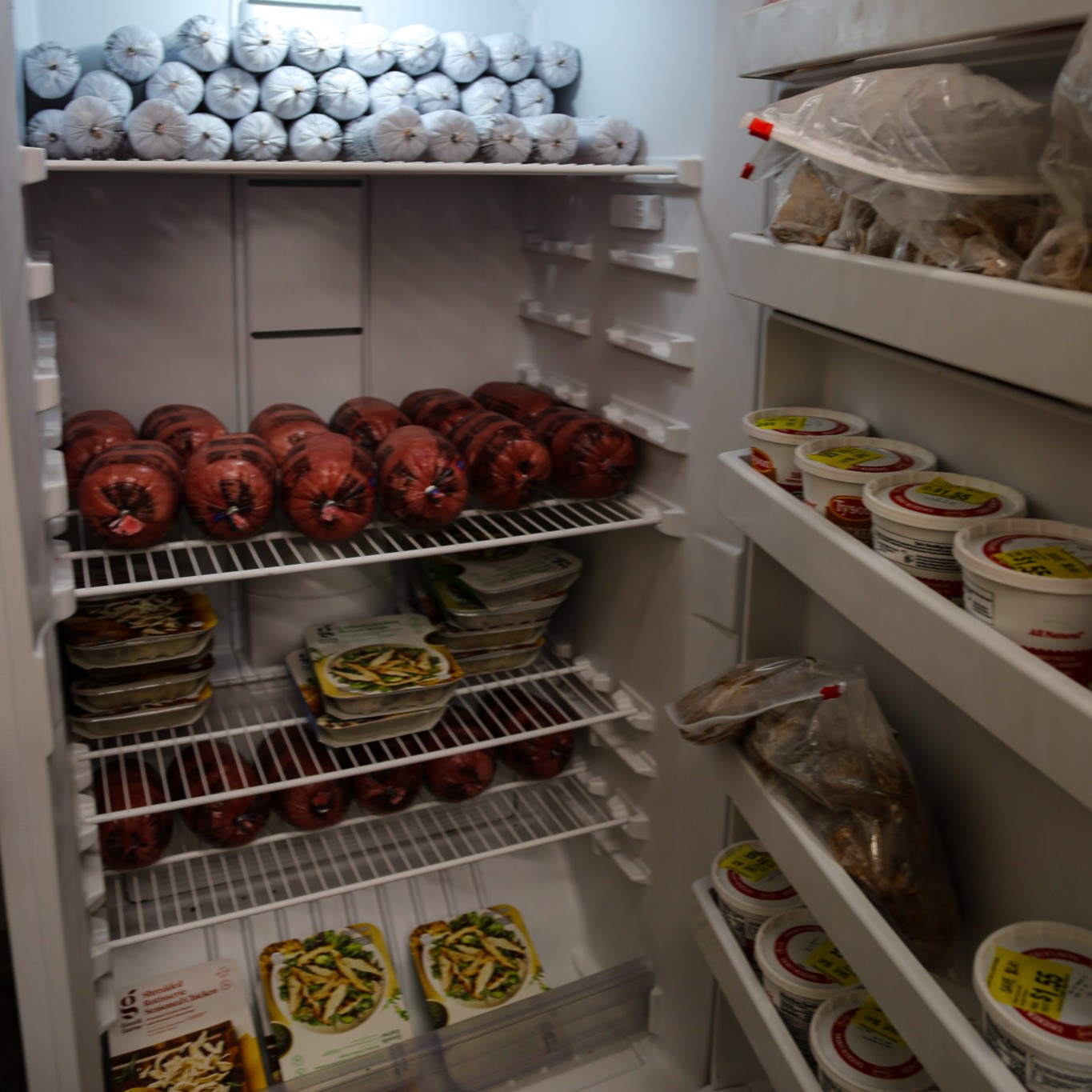 open refrigerator with stacks of ground meat and frozen meals at food pantry